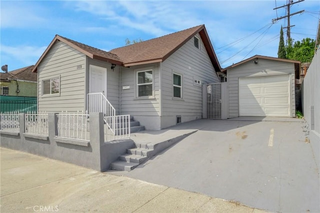 view of front of property featuring an outbuilding, concrete driveway, fence, and roof with shingles