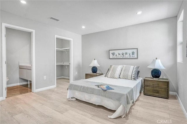 bedroom featuring a spacious closet, ensuite bath, light wood-style flooring, baseboards, and recessed lighting