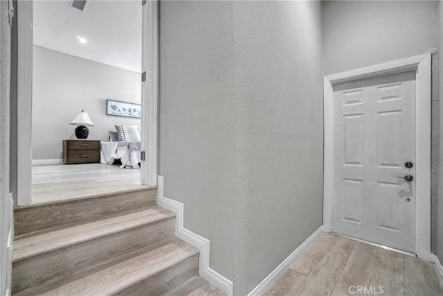 entryway with baseboards, a textured wall, wood finished floors, and stairs