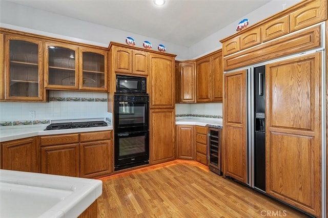 kitchen with brown cabinets, glass insert cabinets, light wood finished floors, and black appliances