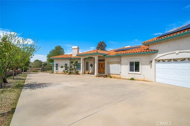 mediterranean / spanish-style house with stucco siding, a chimney, a tiled roof, and concrete driveway