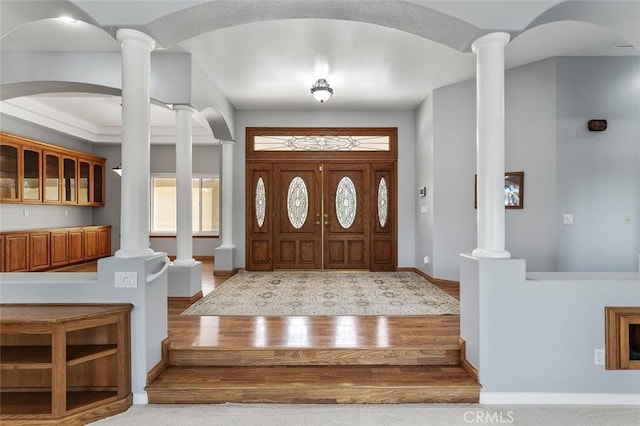 entrance foyer with arched walkways, baseboards, wood finished floors, and decorative columns