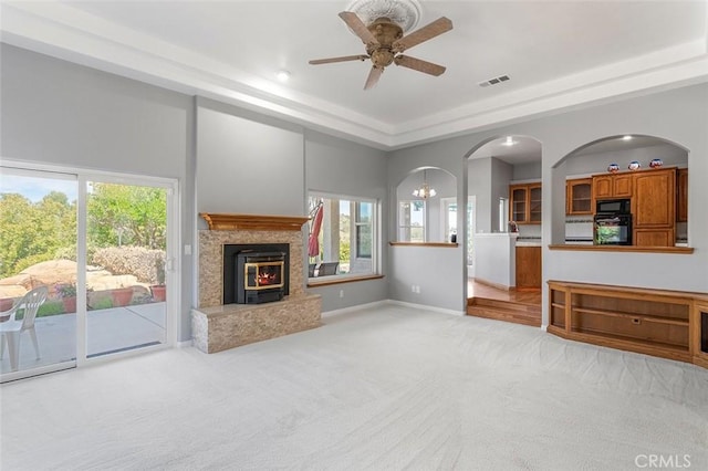 unfurnished living room with light carpet, arched walkways, a wealth of natural light, visible vents, and ceiling fan