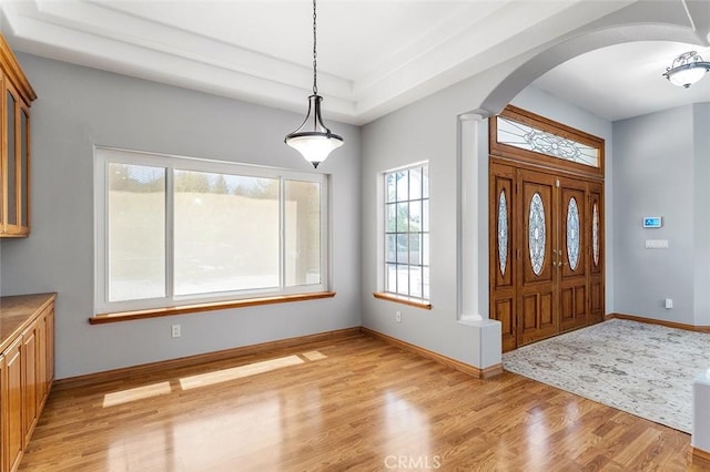 entrance foyer with light wood-style flooring, baseboards, arched walkways, and decorative columns