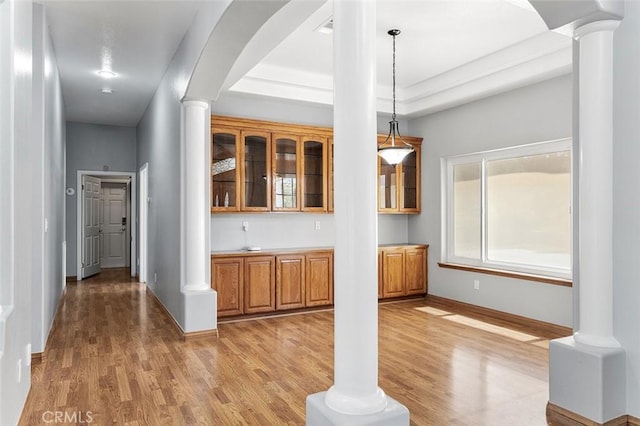 unfurnished dining area with a healthy amount of sunlight, light wood finished floors, and decorative columns