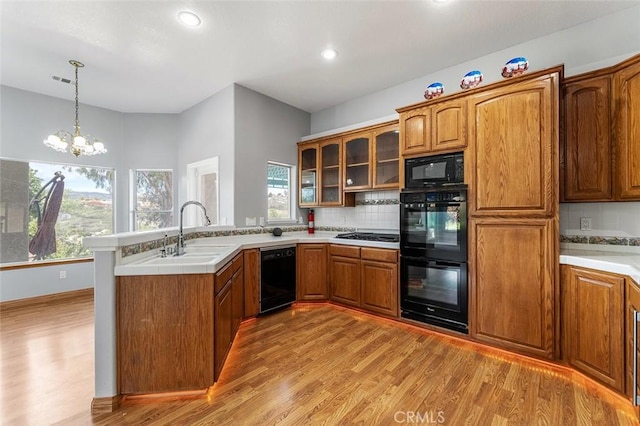 kitchen featuring brown cabinets, a sink, light wood-type flooring, black appliances, and a peninsula