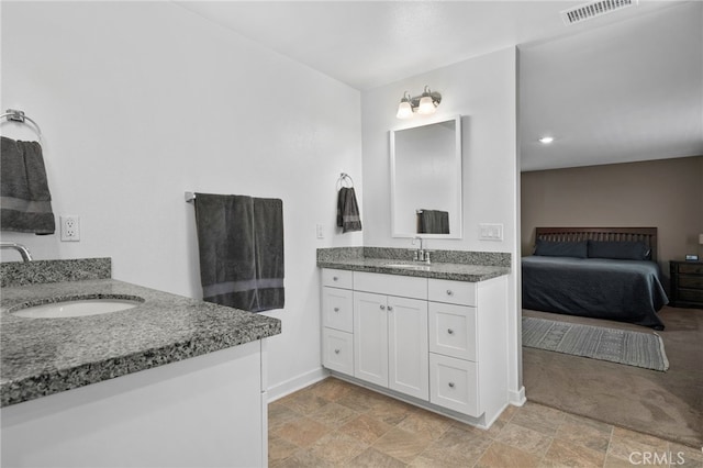ensuite bathroom featuring stone finish flooring, baseboards, a sink, and visible vents