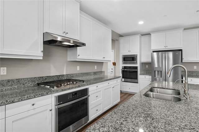 kitchen with under cabinet range hood, stainless steel appliances, a sink, dark stone counters, and white cabinetry