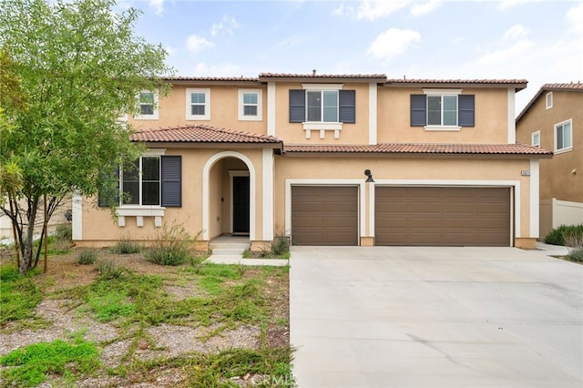 mediterranean / spanish house with concrete driveway, an attached garage, a tiled roof, and stucco siding