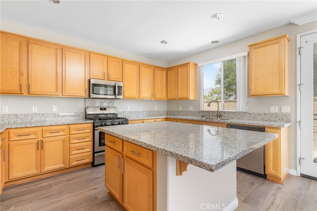 kitchen featuring light stone countertops, appliances with stainless steel finishes, a sink, a center island, and light wood-type flooring