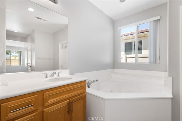 bathroom featuring a healthy amount of sunlight, vanity, a garden tub, and visible vents