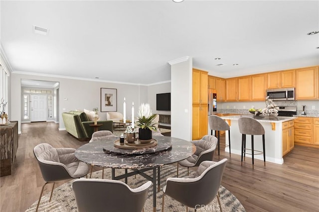 dining room featuring visible vents, ornamental molding, light wood-style flooring, and baseboards