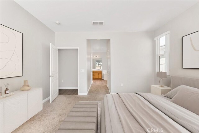 bedroom featuring baseboards, light colored carpet, ensuite bath, and visible vents