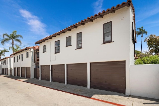 view of side of home featuring stucco siding, a tile roof, and an attached garage