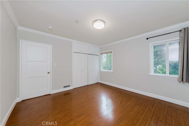 unfurnished bedroom featuring baseboards, ornamental molding, wood finished floors, and a closet