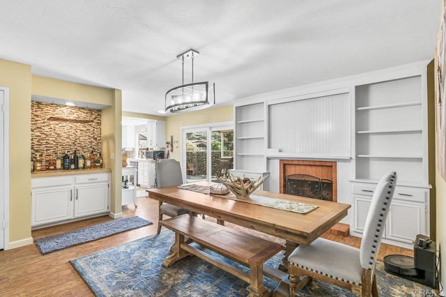 dining room featuring baseboards, a fireplace, light wood-type flooring, and a notable chandelier