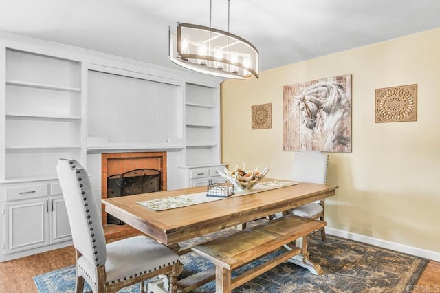 dining room featuring wood finished floors, a fireplace, baseboards, a chandelier, and built in shelves