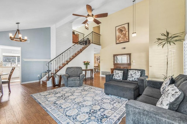 living room with high vaulted ceiling, ceiling fan with notable chandelier, hardwood / wood-style floors, visible vents, and stairway