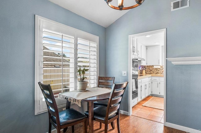 dining area featuring visible vents, baseboards, lofted ceiling, an inviting chandelier, and light wood-style flooring