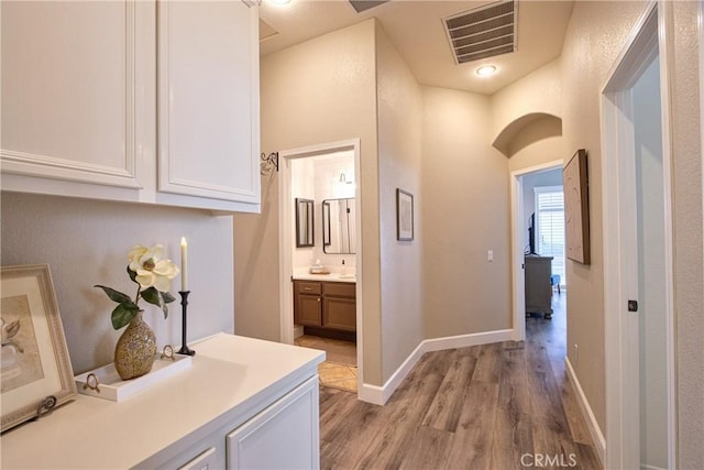 hallway with visible vents, light wood-style flooring, and baseboards