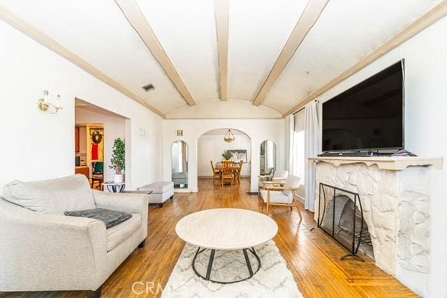 6114 Allston St, Los Angeles, CA 90022 - living area with arched walkways, vaulted ceiling with beams, visible vents, a premium fireplace, and wood finished floors