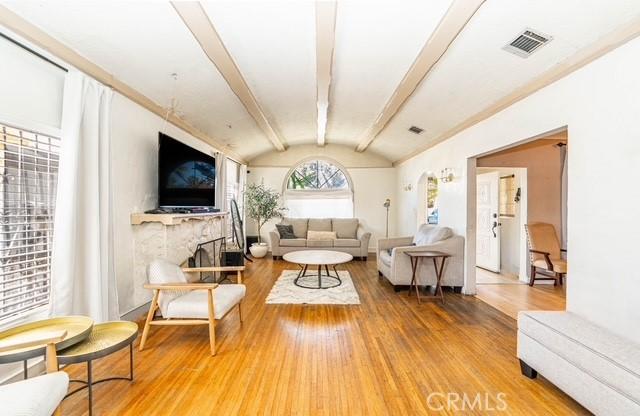 6114 Allston St, Los Angeles, CA 90022 - living room with wood finished floors, vaulted ceiling with beams, visible vents, and a fireplace