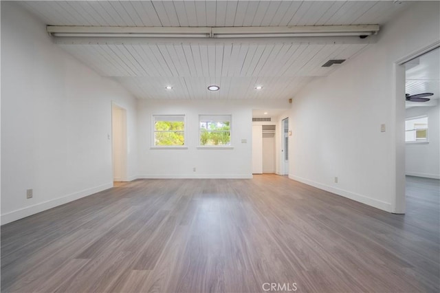 empty room featuring beamed ceiling, visible vents, a wealth of natural light, and wood finished floors