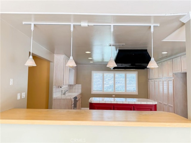 kitchen with a peninsula, a sink, recessed lighting, decorative backsplash, and tile counters