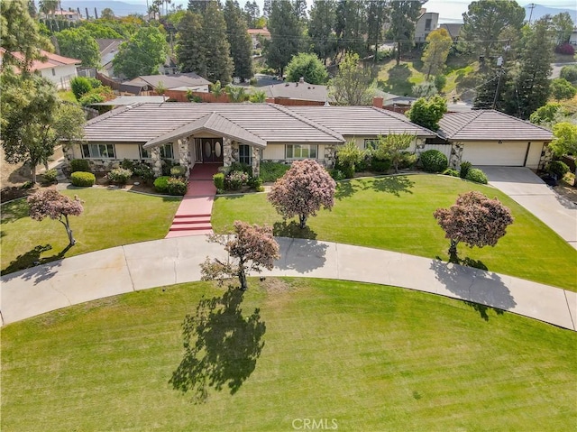 view of front facade featuring a tile roof, stone siding, a front yard, and concrete driveway