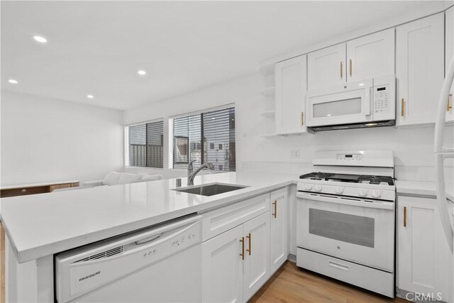 kitchen with a peninsula, white appliances, a sink, and white cabinetry