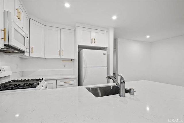 kitchen with a sink, white appliances, white cabinets, light stone countertops, and recessed lighting