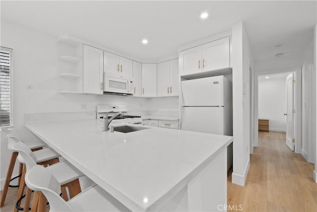 kitchen with a peninsula, light countertops, white cabinets, and white appliances