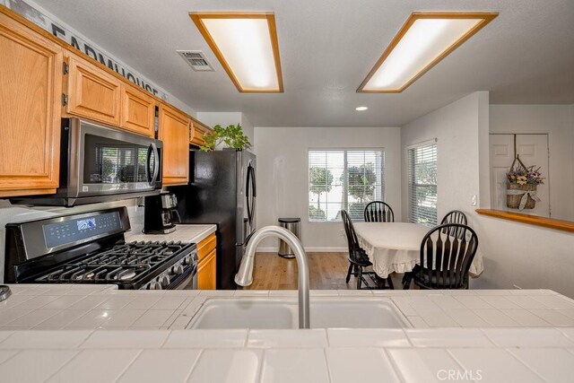 6030 Treehaven Ct, Lancaster, CA 93536 - kitchen featuring appliances with stainless steel finishes, tile countertops, a sink, wood finished floors, and recessed lighting
