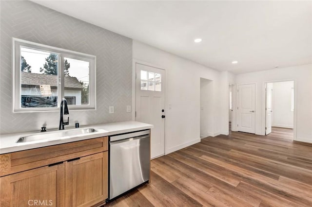 kitchen featuring light wood finished floors, stainless steel dishwasher, light countertops, and a sink