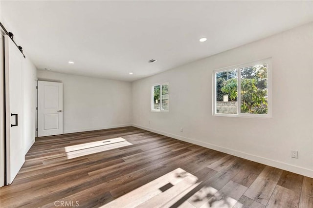 spare room featuring recessed lighting, a barn door, wood finished floors, visible vents, and baseboards