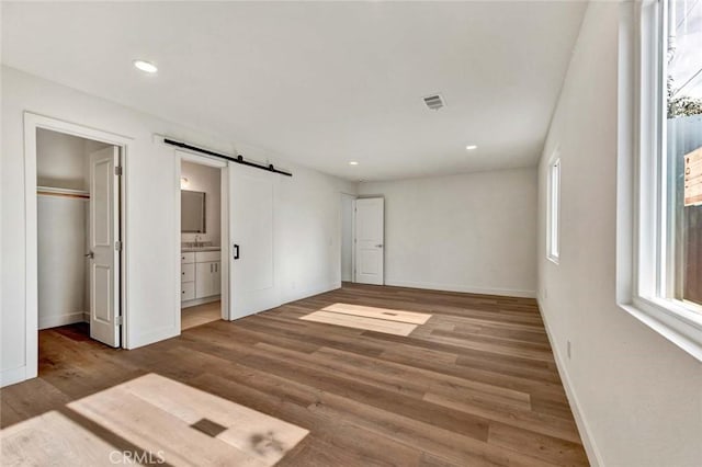 unfurnished bedroom featuring a barn door, wood finished floors, a spacious closet, baseboards, and visible vents