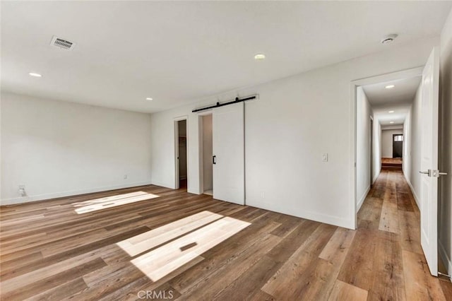 spare room featuring a barn door, wood finished floors, baseboards, visible vents, and recessed lighting