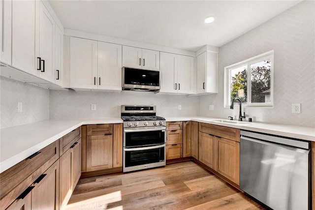 kitchen with backsplash, light countertops, a sink, light wood-style floors, and appliances with stainless steel finishes
