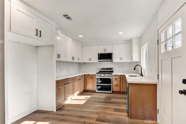 kitchen featuring light wood finished floors, stainless steel appliances, a sink, tasteful backsplash, and visible vents