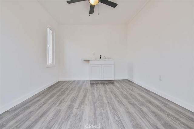 spare room featuring ceiling fan, baseboards, wood finished floors, and a sink