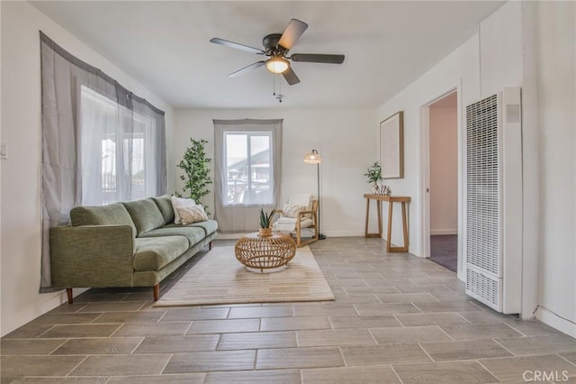 living area featuring wood finish floors, a ceiling fan, baseboards, and a heating unit