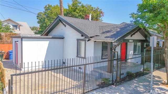 bungalow with roof with shingles, a chimney, and a fenced front yard