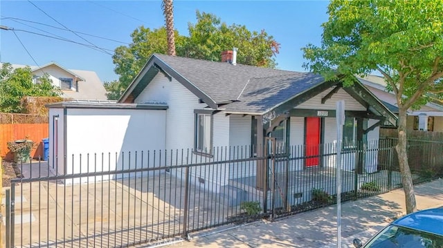 bungalow-style house with a chimney, a shingled roof, and a fenced front yard