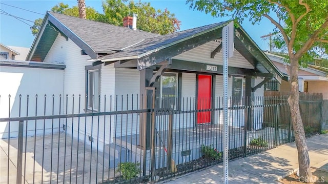 bungalow-style home featuring a chimney, a gate, roof with shingles, and a fenced front yard