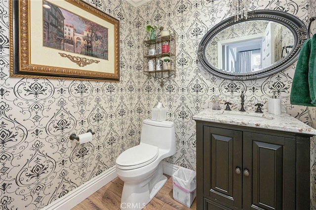 bathroom featuring wallpapered walls, wood finished floors, toilet, vanity, and baseboards