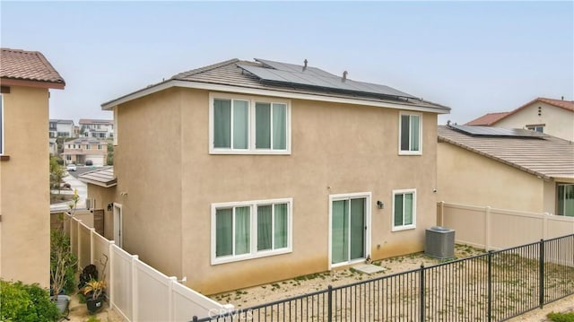 back of house featuring cooling unit, roof mounted solar panels, a fenced backyard, and stucco siding