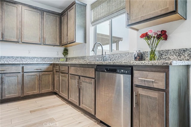 kitchen featuring light stone counters, a sink, light wood-style floors, and dishwasher