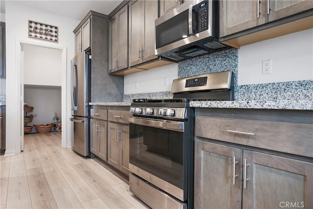kitchen with dark brown cabinets, light stone counters, light wood-style flooring, stainless steel appliances, and backsplash