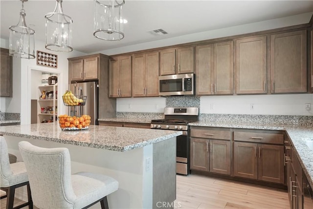 kitchen featuring stainless steel appliances, light stone countertops, visible vents, and light wood-style floors
