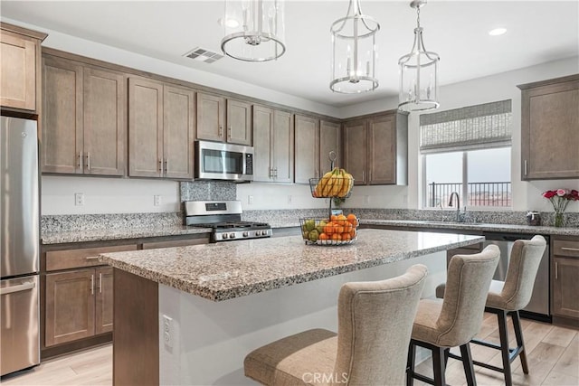 kitchen featuring light stone countertops, a kitchen breakfast bar, a center island, stainless steel appliances, and visible vents